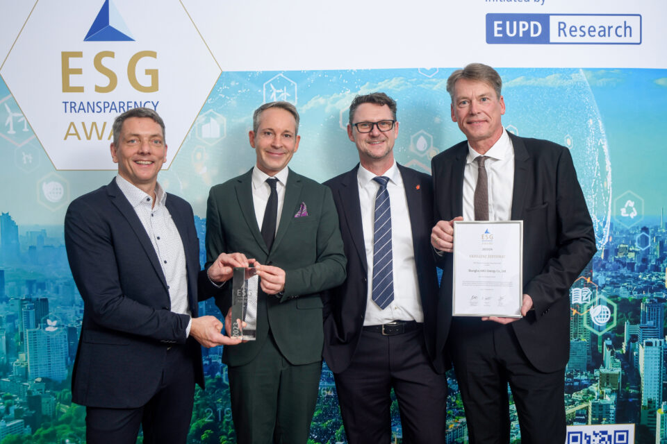 Vier Männer in Anzügen stehen vor einer ESG Transparency Award-Wand, zwei halten eine Trophäe und eine Urkunde