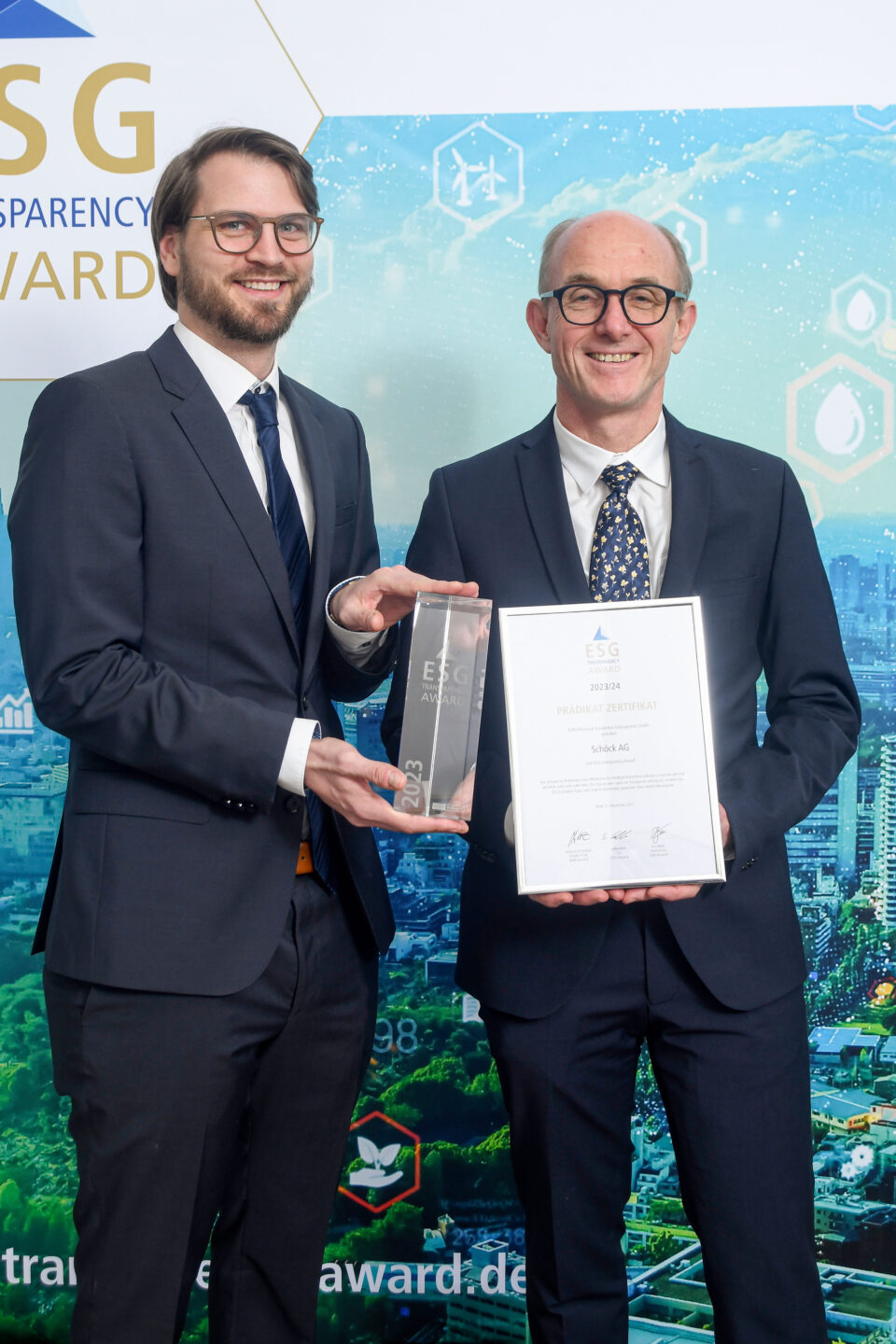 Zwei Männer in Anzügen halten bei der Preisverleihung des ESG Transparency Award eine Trophäe und eine Urkunde vor einem thematisch gestalteten Hintergrund.