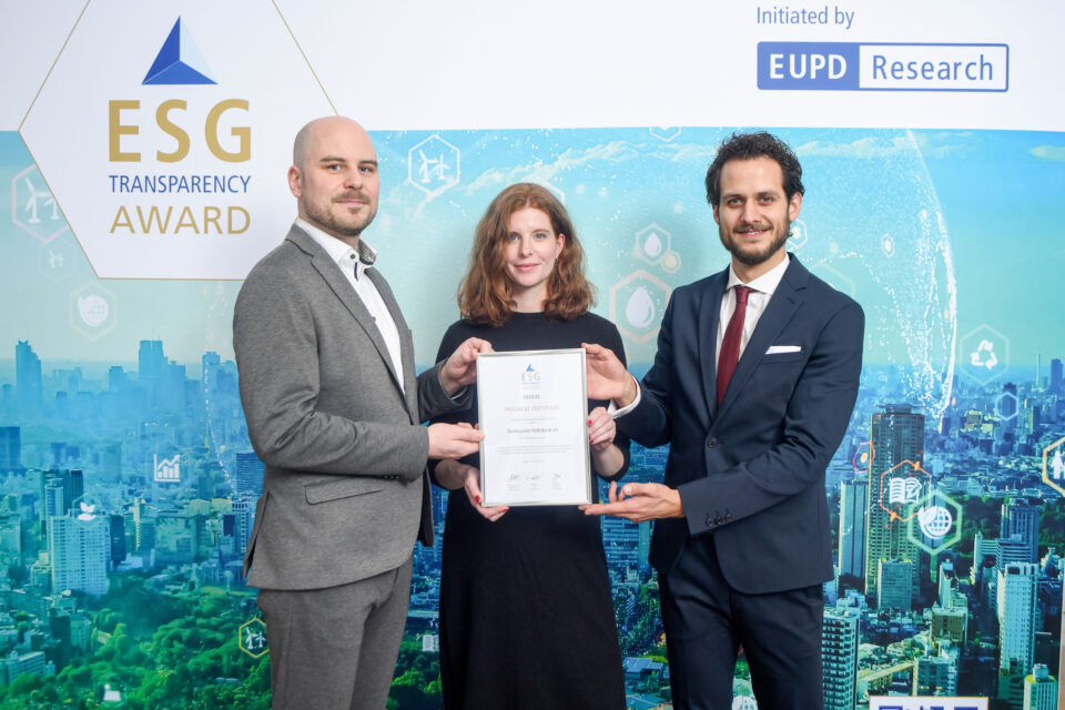 Drei Personen stehen vor einer Wand mit dem Schriftzug 'ESG Transparency Award' und halten gemeinsam eine Urkunde
