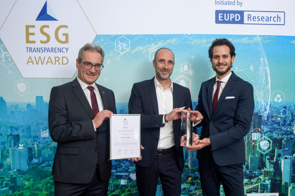 Drei Männer in Anzügen stehen vor einer ESG Transparency Award-Wand, zwei halten eine Urkunde und eine Auszeichnung
