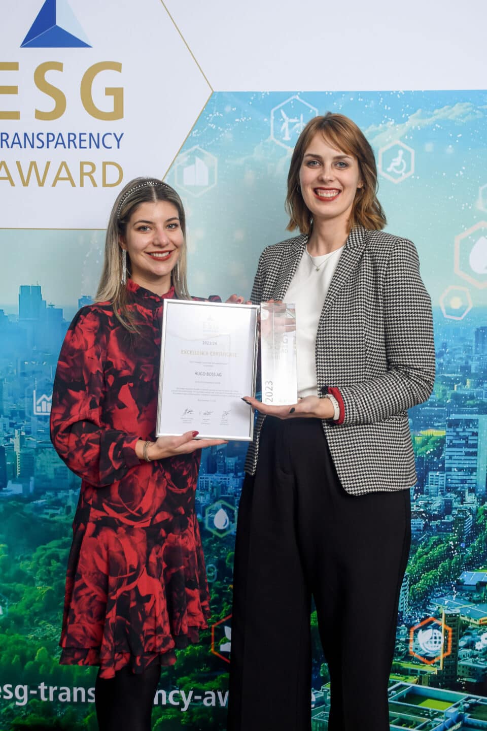 Zwei Frauen stehen vor einer ESG Transparency Award-Wand, eine hält eine Urkunde, die andere eine gläserne Trophäe