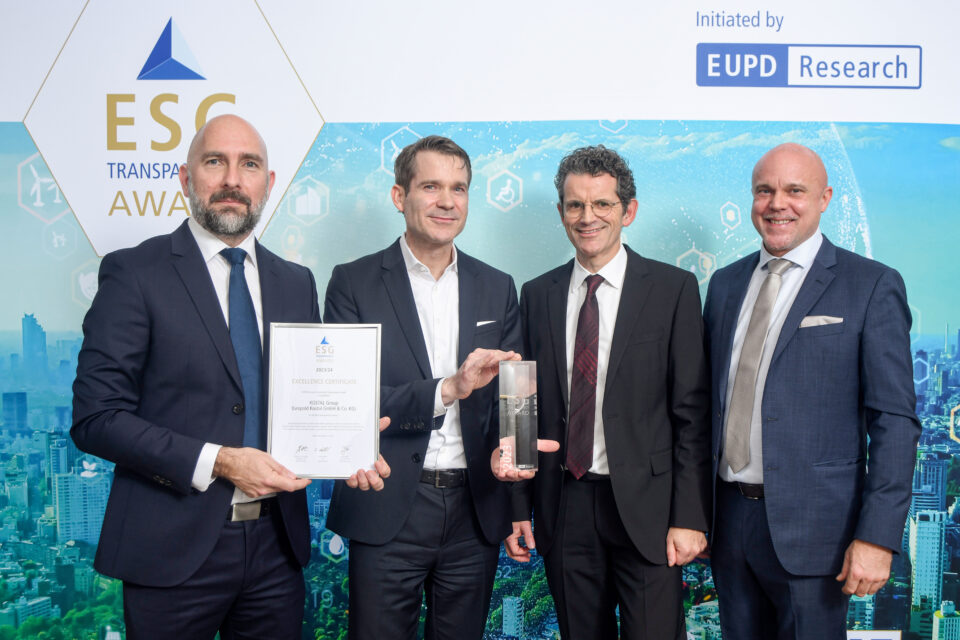 Vier Männer in Anzügen stehen vor einer Wand mit dem Schriftzug 'ESG Transparency Award' und halten eine Urkunde sowie einen gläsernen Preis.