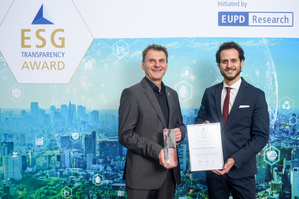 Zwei Männer in Anzügen stehen vor einer blauen Wand mit ESG Transparency Award-Logo, einer hält eine Trophäe, der andere eine Urkunde