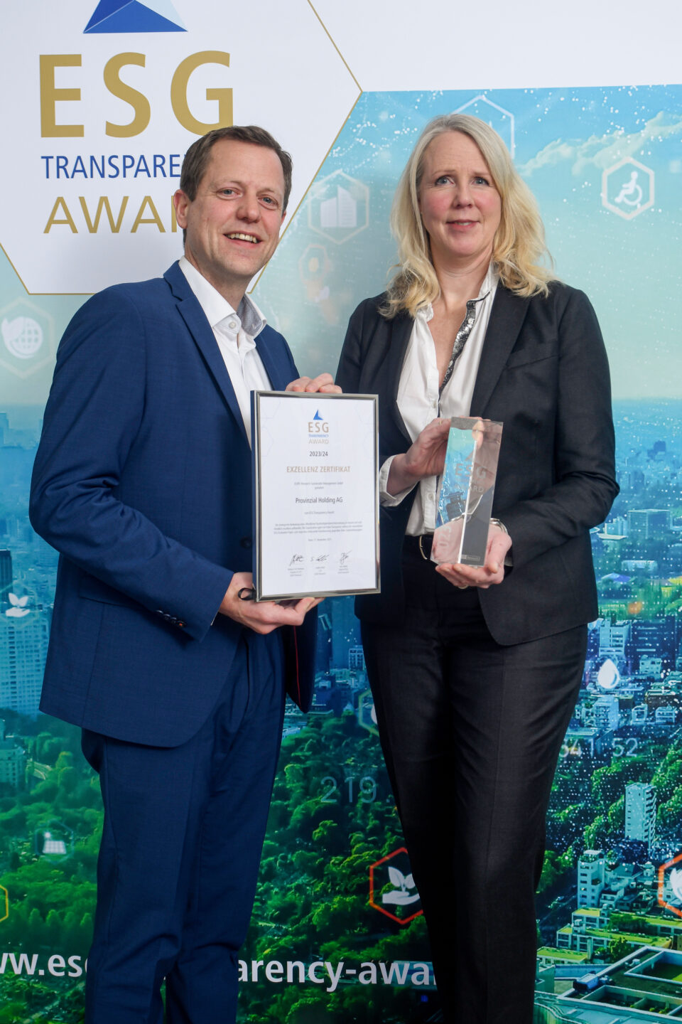 Zwei Personen in Businesskleidung halten bei der Preisverleihung des ESG Transparency Award eine Urkunde und eine Trophäe vor einem Hintergrund mit dem ESG Transparency Award-Logo.