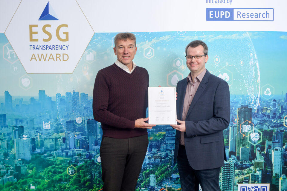 Zwei Männer stehen vor einer Wand mit dem Schriftzug 'ESG Transparency Award' und halten gemeinsam eine Urkunde