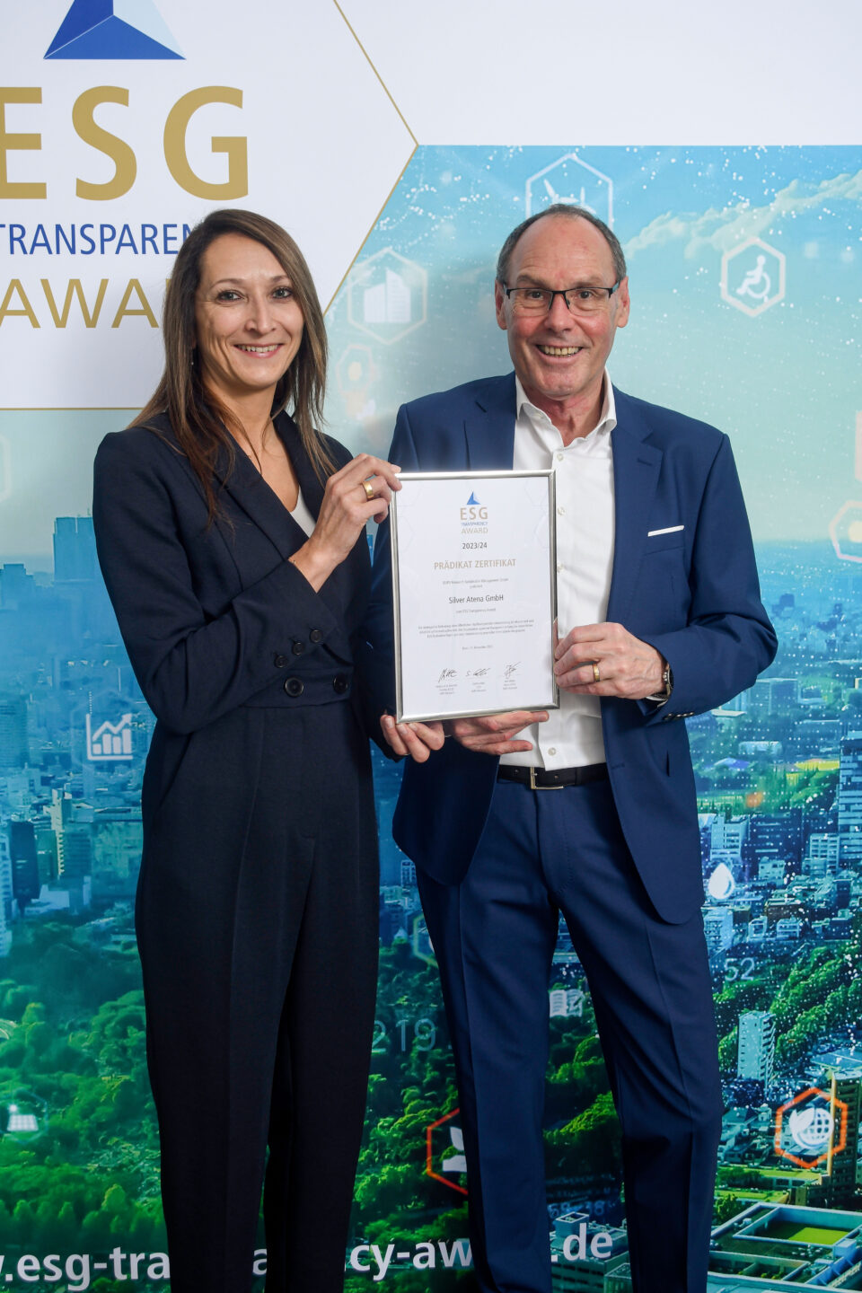 Zwei Personen in formeller Kleidung halten gemeinsam eine Urkunde vor einem ESG Transparency Award-Hintergrund.