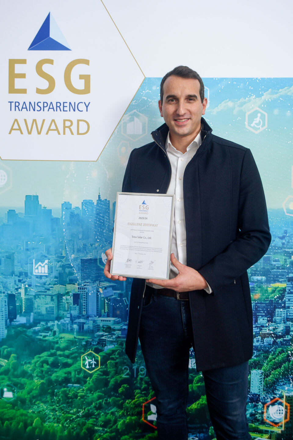 Ein Mann in dunklem Mantel hält eine Urkunde vor einer Wand mit dem Schriftzug 'ESG TRANSPARENCY AWARD' und einer Stadtlandschaft im Hintergrund