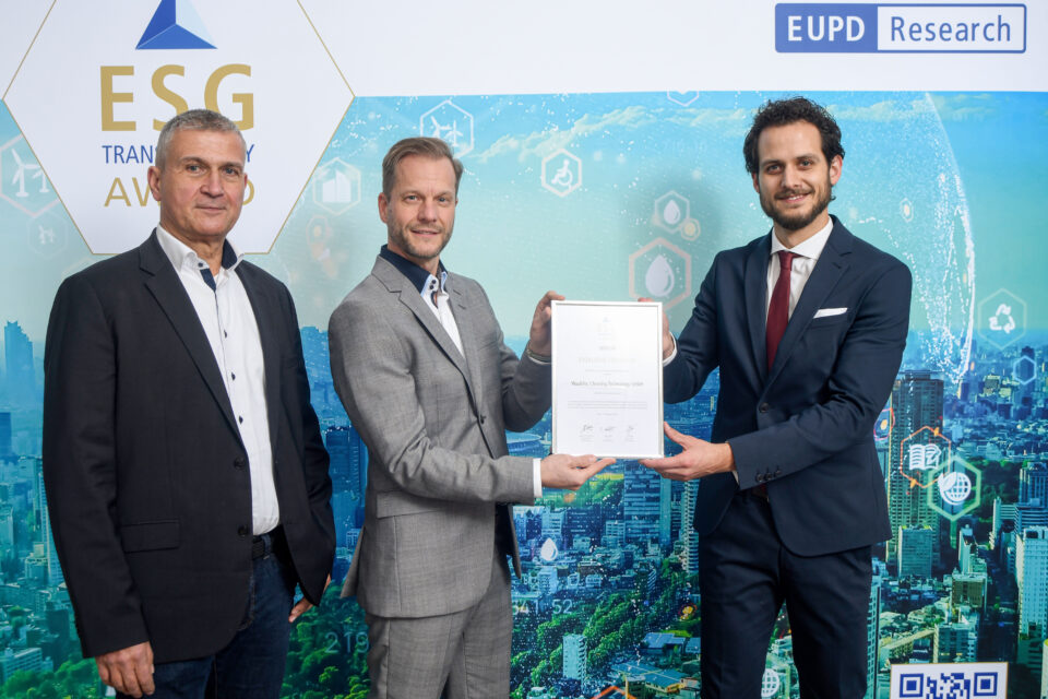 Drei Männer in Anzügen stehen vor einer ESG Transparency Award-Wand, zwei von ihnen halten gemeinsam eine Urkunde